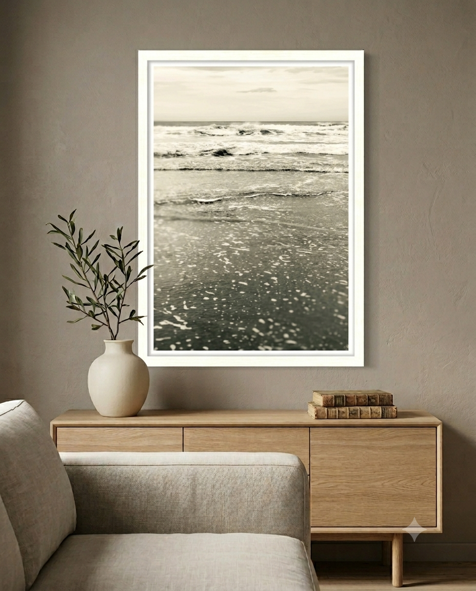Black and white ocean wave print in a white frame above a light wood sideboard console.