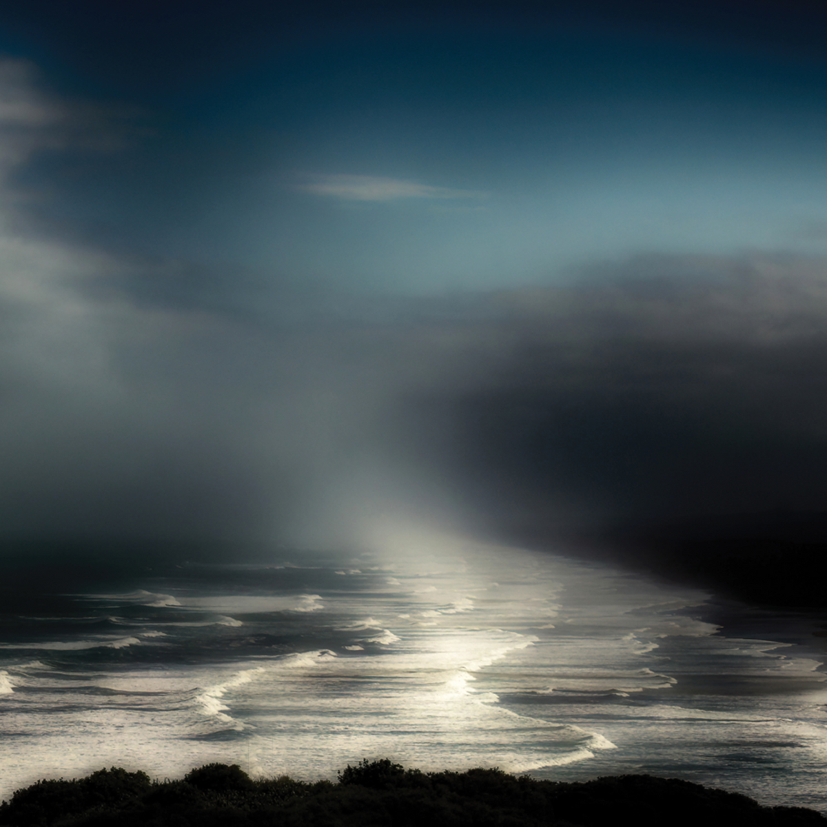 Moody landscape photograph of sunlight breaking through dark storm clouds over ocean waves by Jon Cooper.