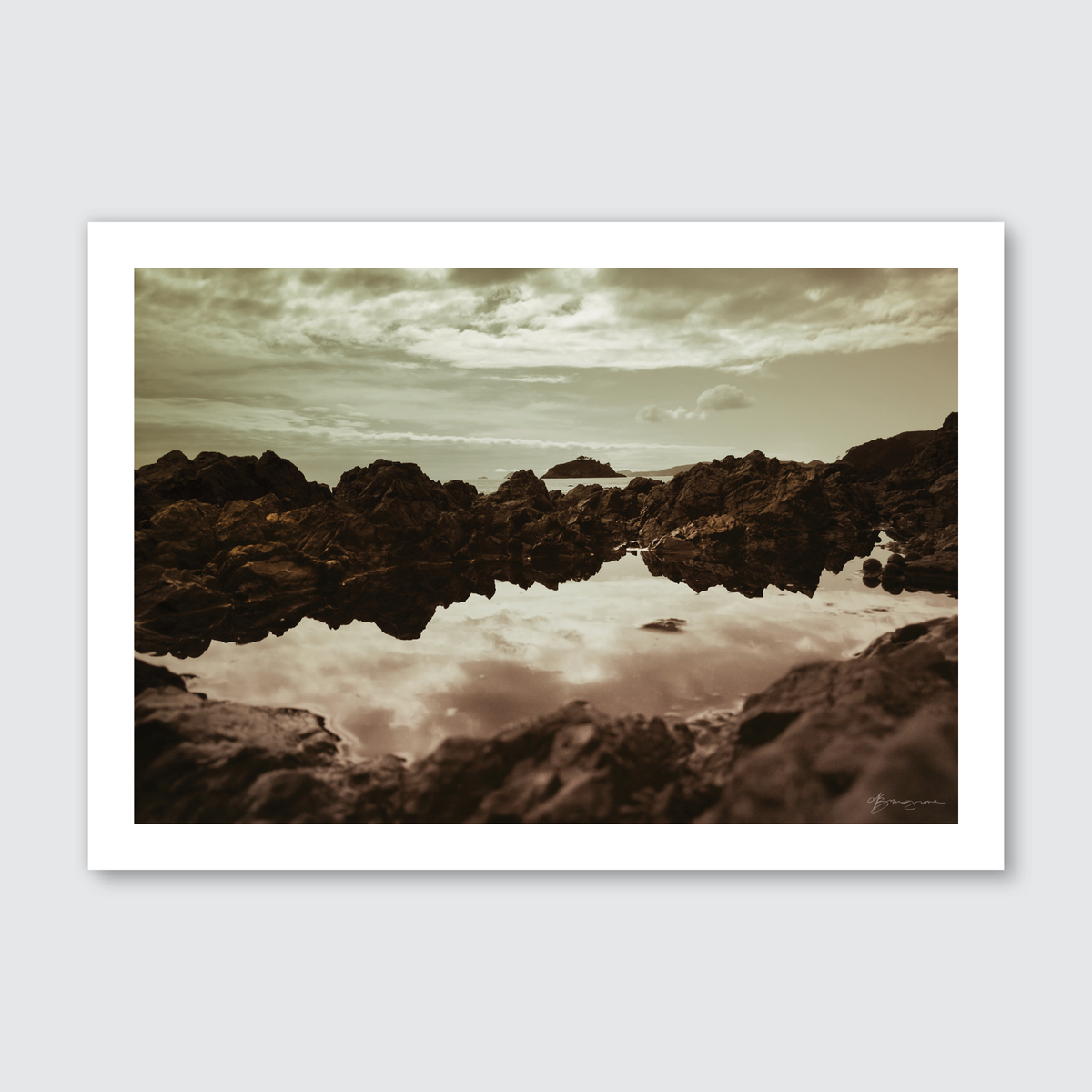 A photograph depicting a moody and serene seascape in New Zealand with reflections of clouds and rocks in the water, in a brown monochrome color palette.