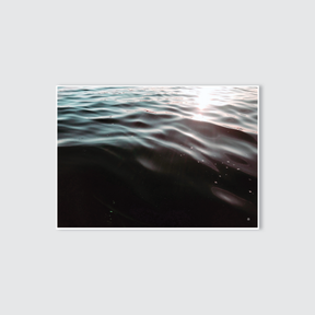 A serene photograph of a body of water with light reflections on the surface, converted into a black and white image.