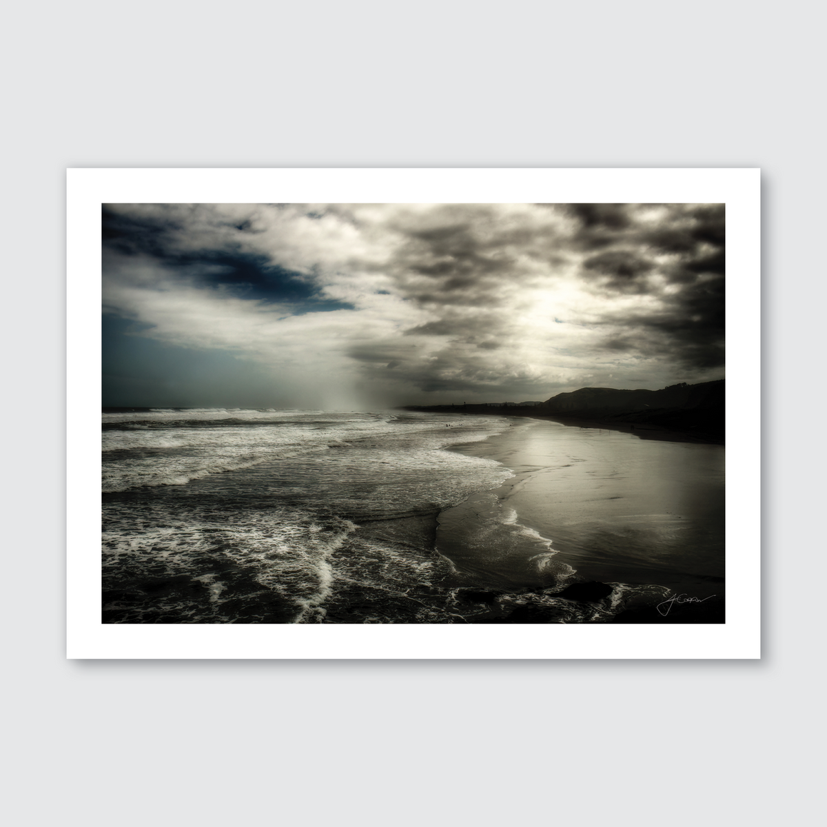 A black and white photograph of Muriwai Beach featuring the rugged sea with waves, a cloudy sky, and a remote coastal terrain.