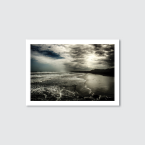 Framed photograph of a landscape with a body of water and mountains under a cloudy sky.