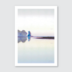 A photograph featuring Piha Beach, New Zealand with a tranquil body of water, rock formation in the background, reflecting in the water's surface under a light blue sky.